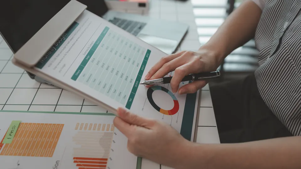Illustrative photo: Hands reviewing printed tables and charts on a desk.