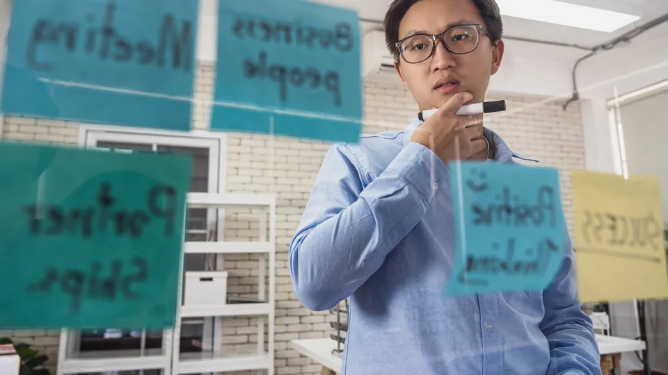 Illustrative photo: Man thinking beside a glass wall covered with planning notes.