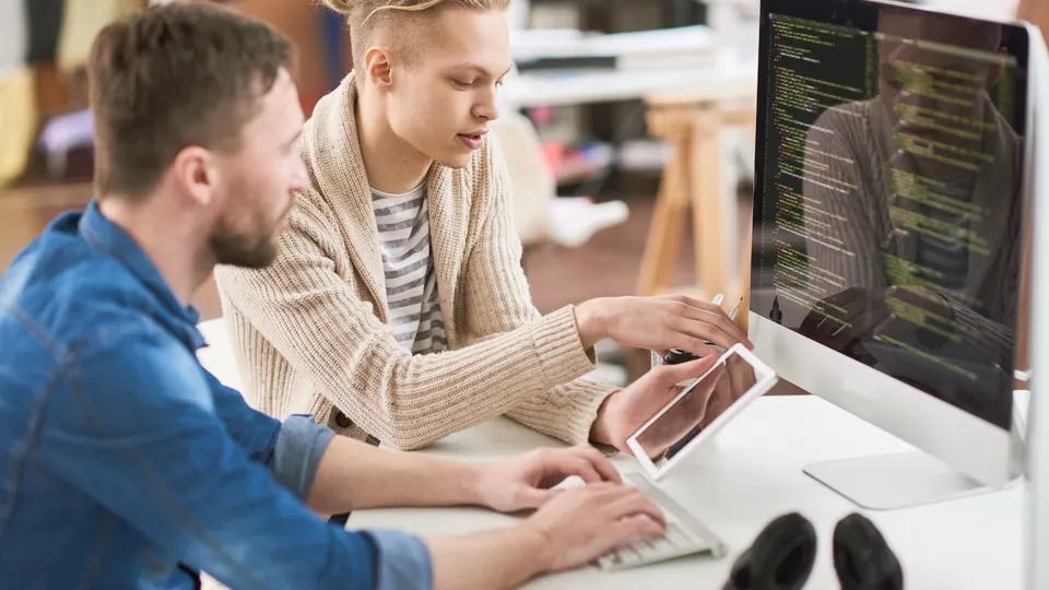 Illustrative photo: Two developers discussing code at a desktop workstation.