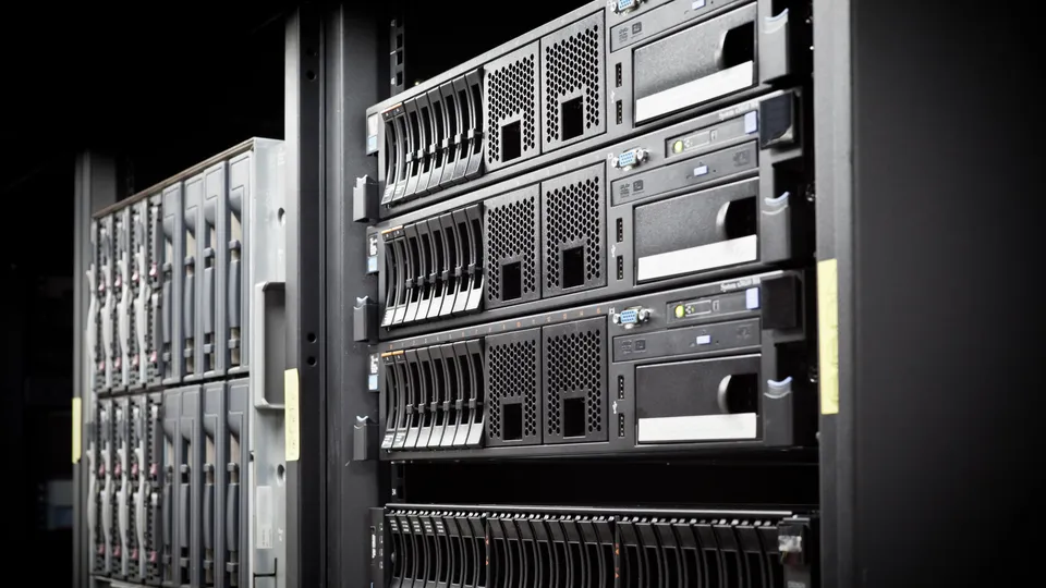 Illustrative photo: Rows of server cabinets in a dark data center.