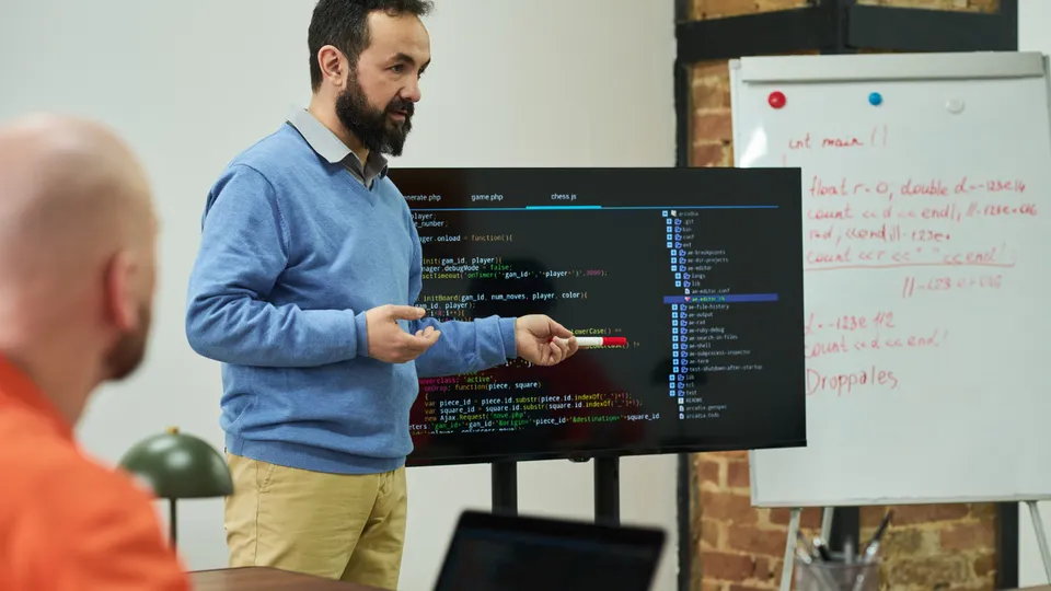 Illustrative photo: Developer explaining source code on a large display to colleagues.