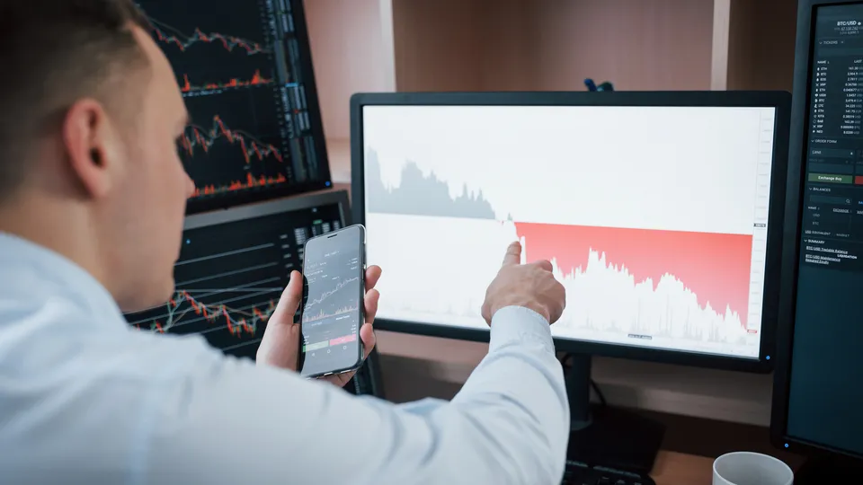 Illustrative photo: Analyst reviewing financial charts across several screens.