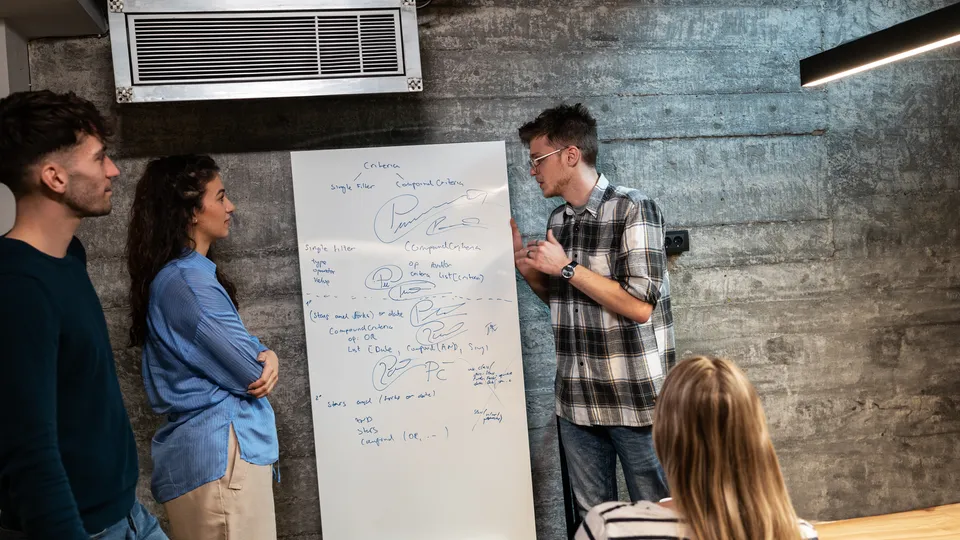 Illustrative photo: Colleagues discussing notes on a whiteboard.