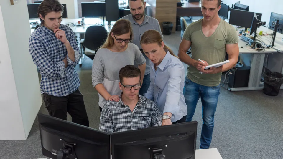 Illustrative photo: Software team gathered around a colleague at a computer.