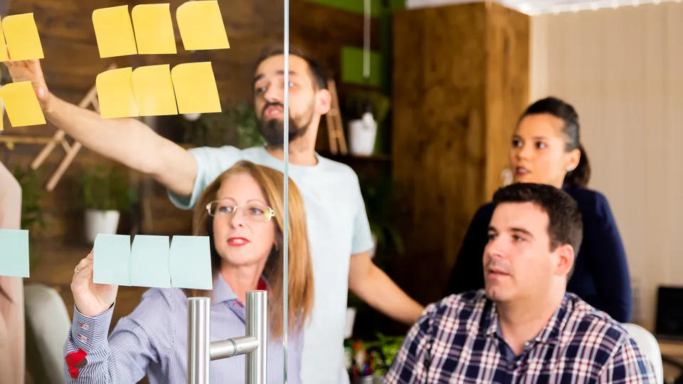 Illustrative photo: Team arranging sticky notes together on a glass wall.