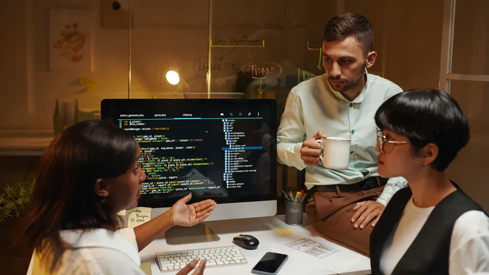Illustrative photo: Developers discussing source code displayed on a monitor.
