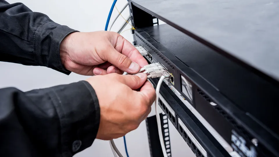 Illustrative photo: Hands connecting network cables to rack equipment.