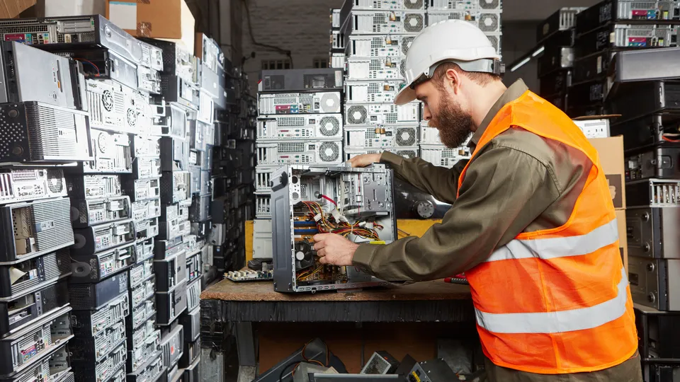 Illustrative photo: Technician handling computer equipment at a recycling facility.