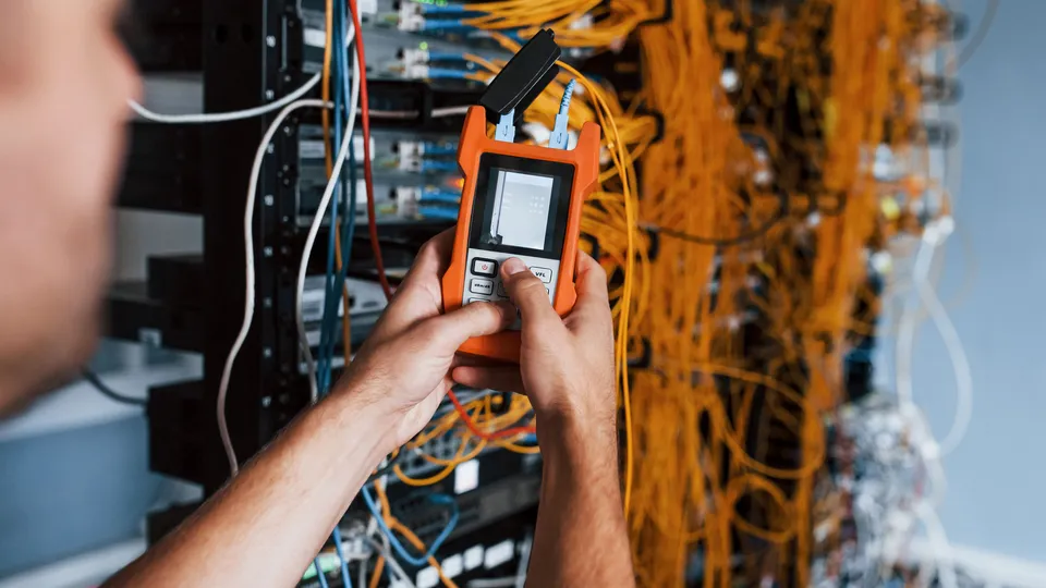 Illustrative photo: Technician holding a cable tester beside network wiring.