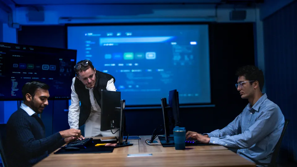 Illustrative photo: Technical team discussing information at computer workstations.