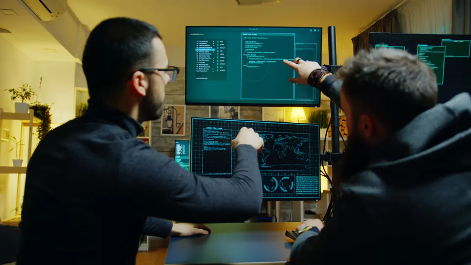 Illustrative photo: Two developers discussing code across several computer screens.