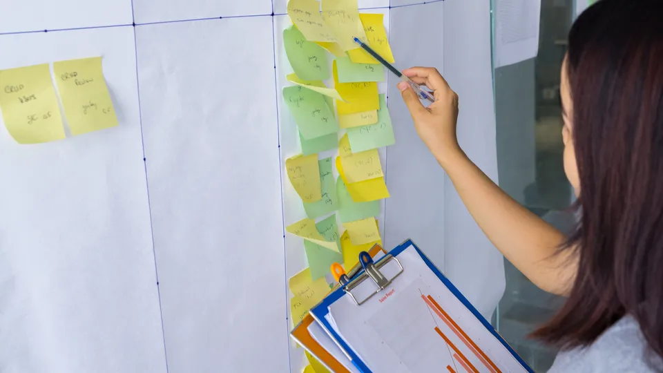 Illustrative photo: Woman moving sticky notes on a task board.