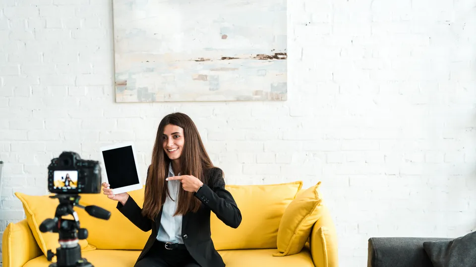 Illustrative photo: Woman presenting a tablet to a camera on a tripod.