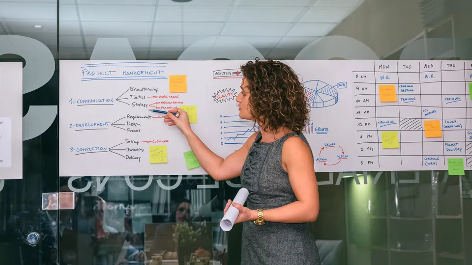 Illustrative photo: Woman presenting a project plan on a large board.
