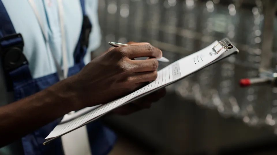 Illustrative photo: Worker checking a list beside industrial equipment.
