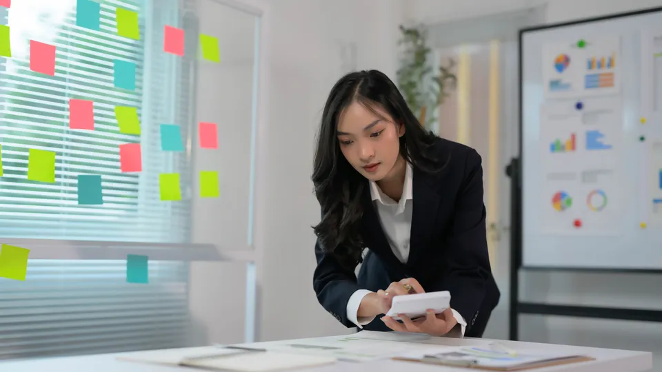 Illustrative photo: Woman using a calculator at an office desk.